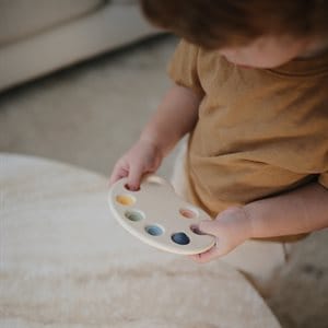 Dziecko trzymające plastikową paletę do zabawy z kolorowymi przyciskami do naciskania dla niemowląt. Mushie Paleta Farb Press Toy