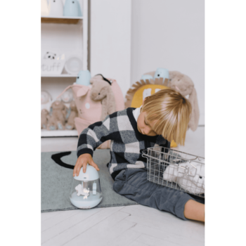 Niebieska lampka z pozytywką w kształcie kurczaczka dla dziecka na podłodze obok chłopca w kratowanej bluzie. Rabbit&Friends Kurczaczek Lampka z Pozytywką Niebieska