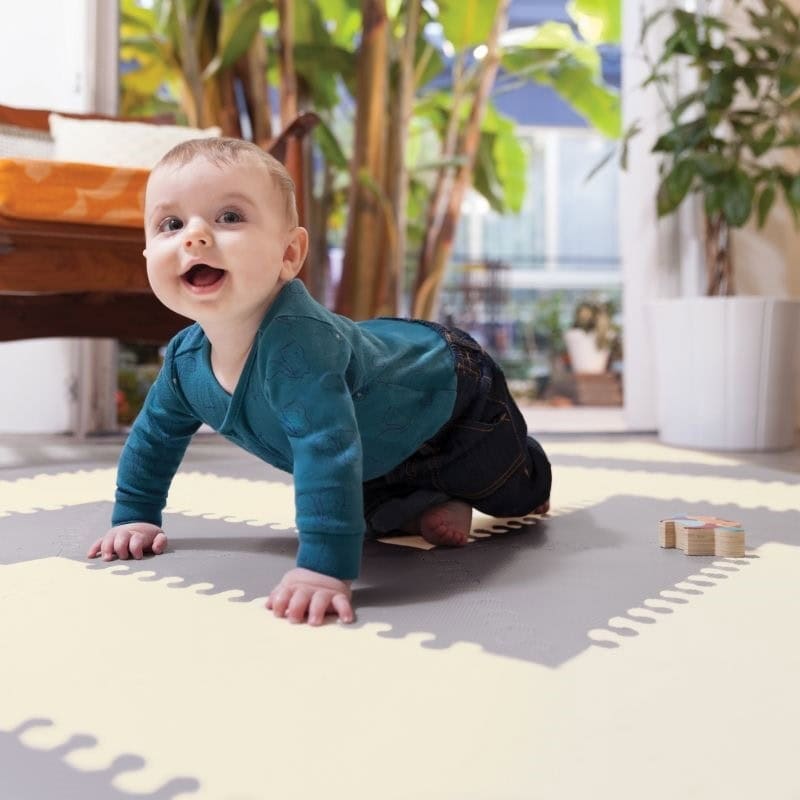Niemowlę raczkujące na szarej piankowej macie z geometrycznym wzorem w jasnych kolorach w pokoju z roślinami. Skip Hop Mata Playspot Grey/Cream GEO