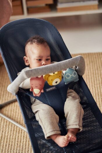Dziecko siedzące w granatowym leżaczku z zawieszoną zabawką z pluszowymi postaciami dla niemowląt. BABYBJORN zabawka do leżaczka Soft Friends