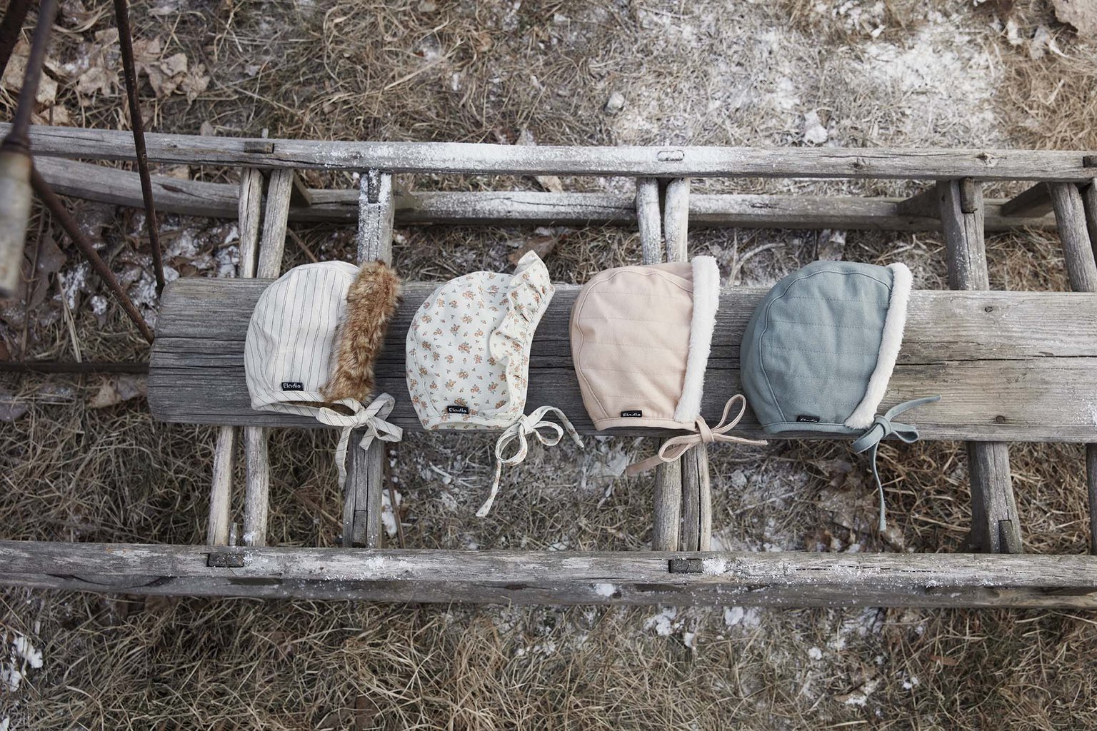 Czapki zimowe dla niemowląt w różnych kolorach i wzorach na drewnianej drabinie. Elodie Details Czapka Winter Bonnet Pinstripe 1-2 lata