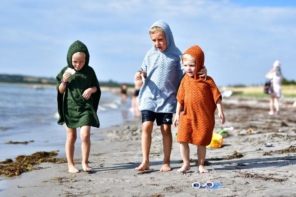 Dzieci na plaży w kąpielowych ponczach z kapturem w kolorach zielonym niebieskim i pomarańczowym. Filibabba Poncho Zigzag Dark Green