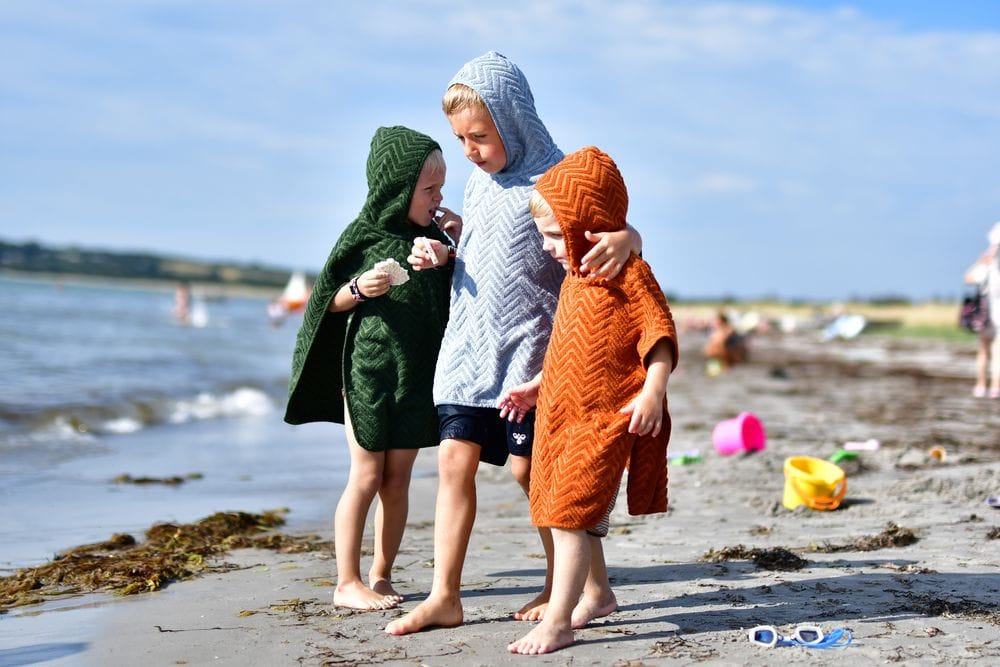 Dzieci na plaży w kąpielowych ponczach z kapturem w kolorach zielonym niebieskim i pomarańczowym. Filibabba Poncho Zigzag Dark Green