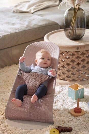 Leżaczek dla niemowlaka ciemny róż z siateczki z dzieckiem siedzącym w pokoju. BABYBJORN leżaczek BLISS MESH Ciemny Róż