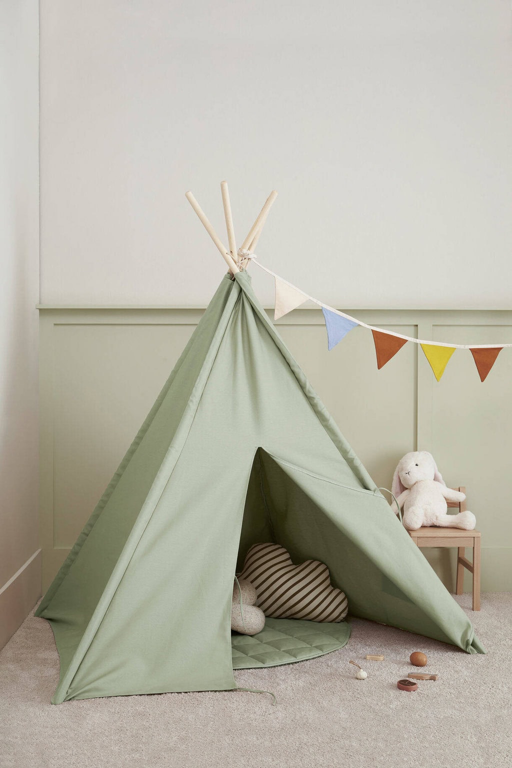 Zielony namiot tipi dla dziecka z drewnianymi kijami i kolorową girlandą w pokoju dziecięcym. Kid’s Concept Namiot Tipi light green