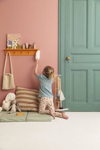 Dziecko sprzątające pokój z zestawem do sprzątania dla dzieci na tle różowej ściany i zielonych drzwi z poduszkami i pluszakami na podłodze. Kid’s Concept Zestaw do sprzątania KID’S HUB