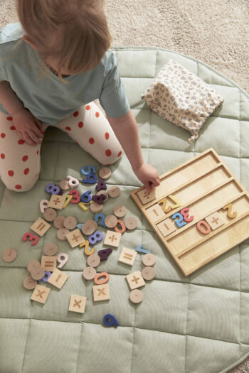 Drewniana tablica kalkulacyjna z kolorowymi cyframi i znakami matematycznymi dla dziecka na miękkim zielonym dywanie. Kid’s Concept Tablica kalkulacyjna