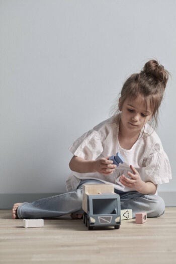 Dziewczynka bawiąca się drewnianą zabawkową śmieciarką i klockami na podłodze. Kid’s Concept Śmieciarka AIDEN