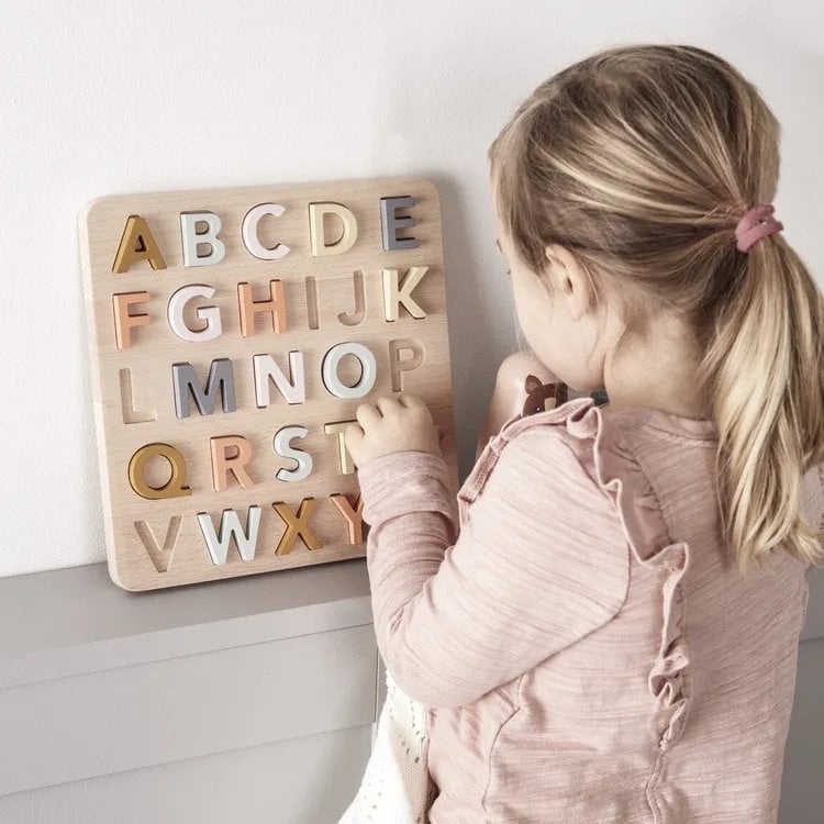 Drewniana układanka z literami alfabetu w pastelowych kolorach dziewczynka układa puzzle. Kid’s Concept Puzzle ABC