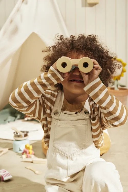 Dziecko bawiące się drewnianymi lornetkami w jasnym pokoju dla małego odkrywcy. Kid’s Concept Zestaw odkrywcy KID’S HUB