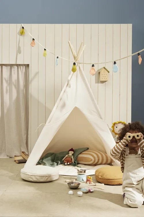 Biały namiot tipi dla dzieci z poduszkami i zabawkami w pokoju dziecięcym z girlandą świetlną i drewnianą dekoracją na ścianie dla małego odkrywcy. Kid’s Concept Zestaw odkrywcy KID’S HUB