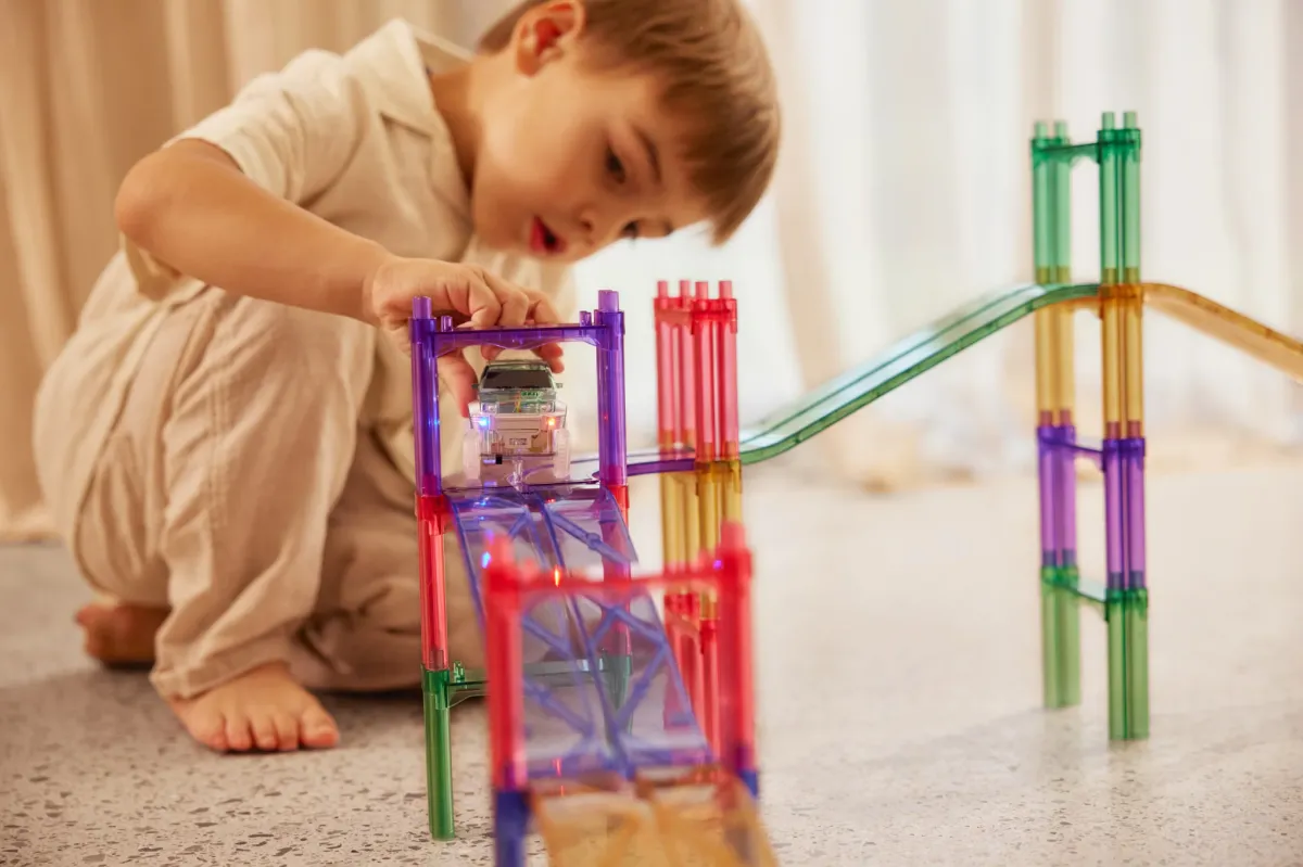 Dziecko bawiące się kolorowymi przezroczystymi klockami magnetycznymi tworzącymi tor wyścigowy. Cleverclixx Klocki magnetyczne Large Race Track Pastel 80 el