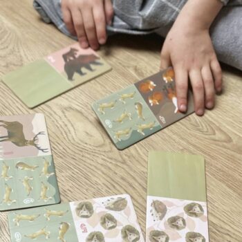 Dziecko układa domino z motywem leśnych zwierząt na drewnianej podłodze. Egmont Toys Domino Leśne Zwierzęta