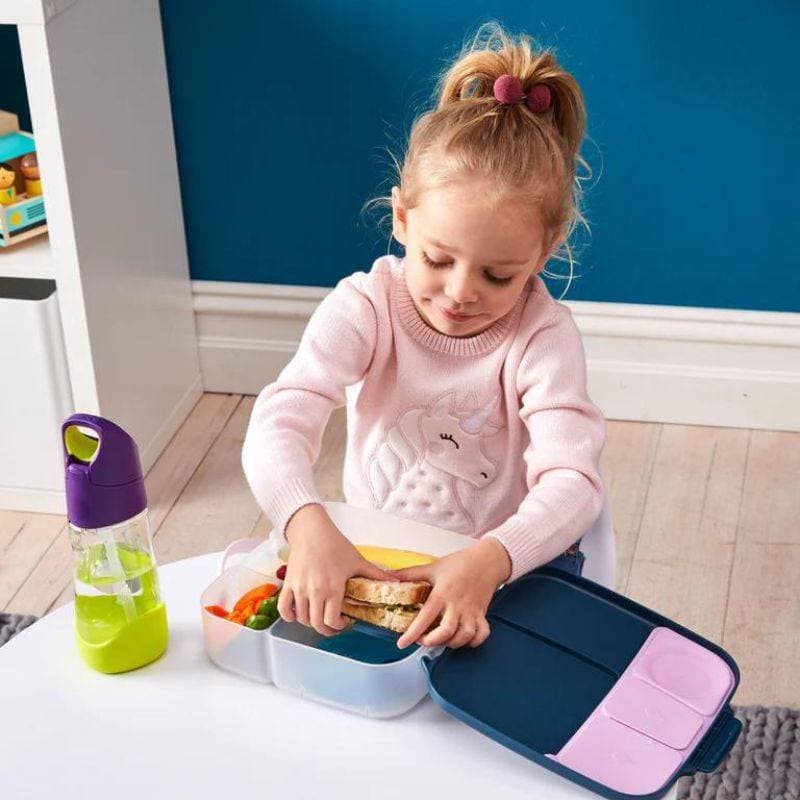 Fioletowa śniadaniówka z przegródkami dla dziecka z kanapką i warzywami obok butelka na napój z zielonym elementem. b.box Lunchbox Lilac Pop