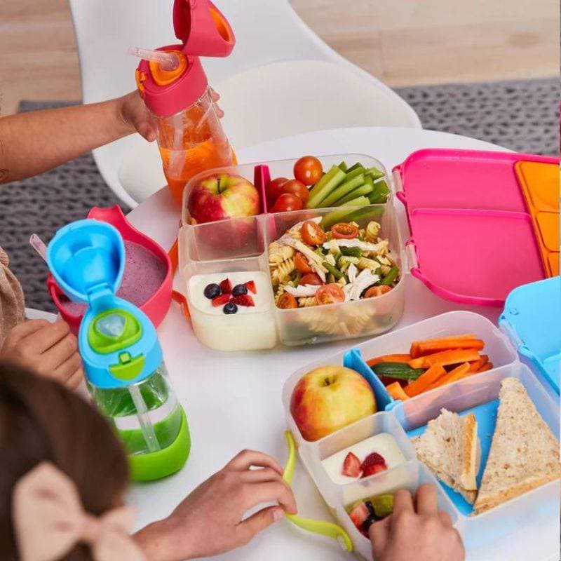 Śniadaniówka z przegródkami różowa z przezroczystym wieczkiem z jedzeniem dla dziecka z bidonem i owocami na stole. b.box Lunchbox Lilac Pop