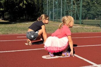 Dwie dziewczynki na torze lekkoatletycznym przygotowujące się do startu w biegu