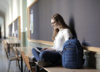 Dziewczyna siedząca na ławce w klasie z plecakiem obok korzystająca z laptopa