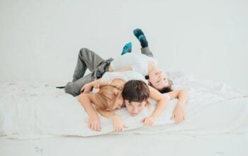 Kobieta w ciąży leżąca na łóżku z dwójką dzieci chłopcem i dziewczynką w skarpetkach
