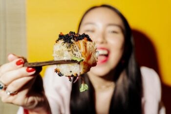 Kobieta trzyma kawałek sushi pałeczkami na żółtym tle