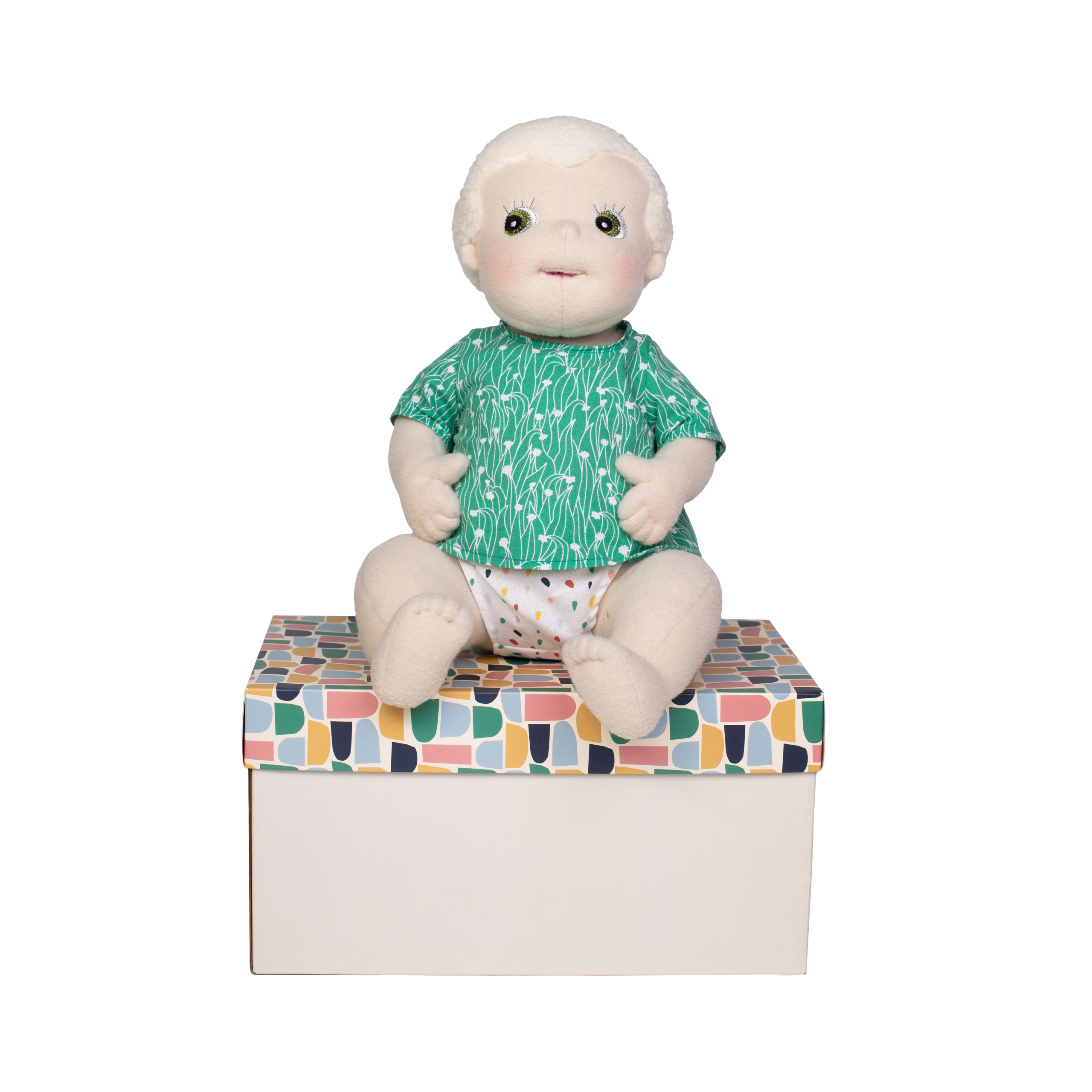 Szmaciana anatomiczna lalka sensoryczna w zielonej bluzce siedząca na pudełku dla dziecka. Rubens Barn Anatomiczna lalka sensoryczna Carl Baby