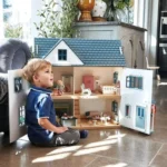 Drewniany trzypiętrowy domek dla lalek z niebieskim dachem i otwieranymi drzwiami chłopiec bawi się przy domku. Tender Leaf Toys Drewniany trzypiętrowy domek dla lalek