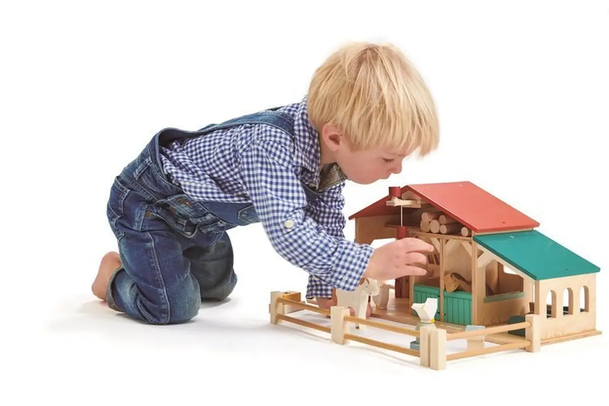 Drewniana farma z figurkami zwierząt i chłopiec bawiący się zabawką dla dzieci. Tender Leaf Toys Drewniane figurki do zabawy farma z zwierzątkami