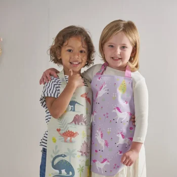 Dwoje dzieci w fartuszkach ochronnych z motywem dinozaurów i jednorożców dla dzieci. ThreadBear Design Fartuszek ochronny Jednorożce