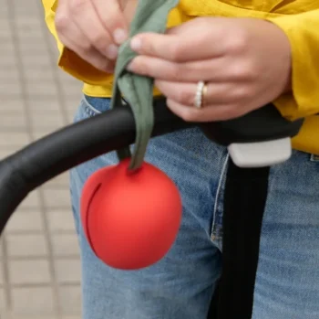 Czerwone silikonowe etui na smoczek w kształcie jabłka z zielonym paskiem dla dziecka zawieszone na rączce wózka. Oli & Carol Etui na Smoczek Jabłko Pepa