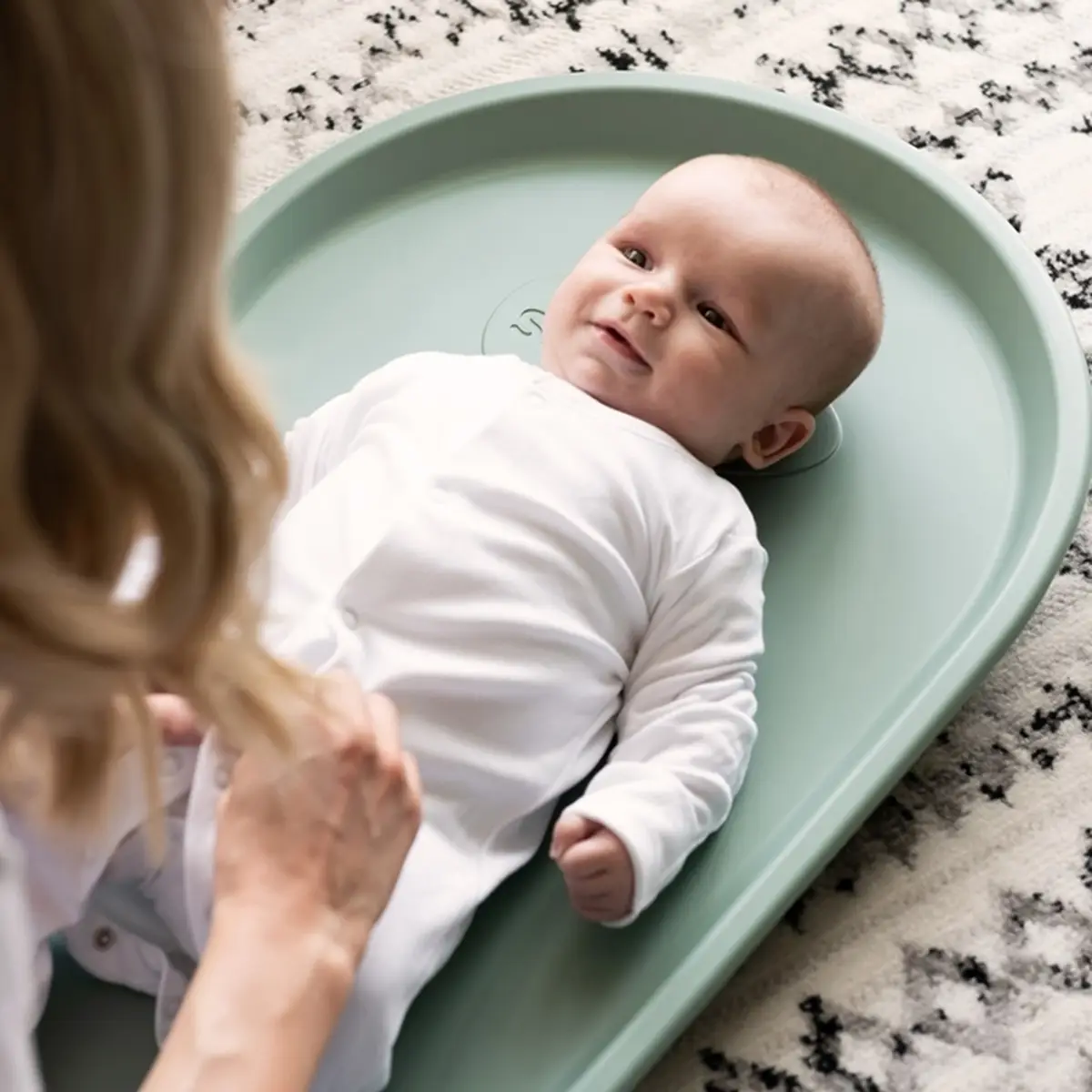 Zielona mata do przewijania z pianki squishy z niemowlakiem ubranego na biało dla dziecka. Shnuggle Mata do Przewijania z Pianki Squishy Eucalyptus