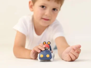 Niebieskie drewniane auto policyjne z figurką kierowcy trzymane przez dziecko w białej koszulce dla dzieci powyżej 6 miesięcy. Tolo Bio Baby auto policyjne 6m+