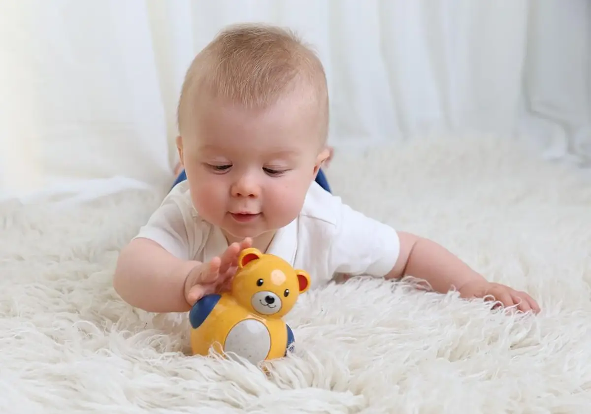 Niemowlę bawiące się żółtym wańka wstańka w kształcie misia na jasnym dywanie. Tolo Bio Miś Roly Poly 6m+