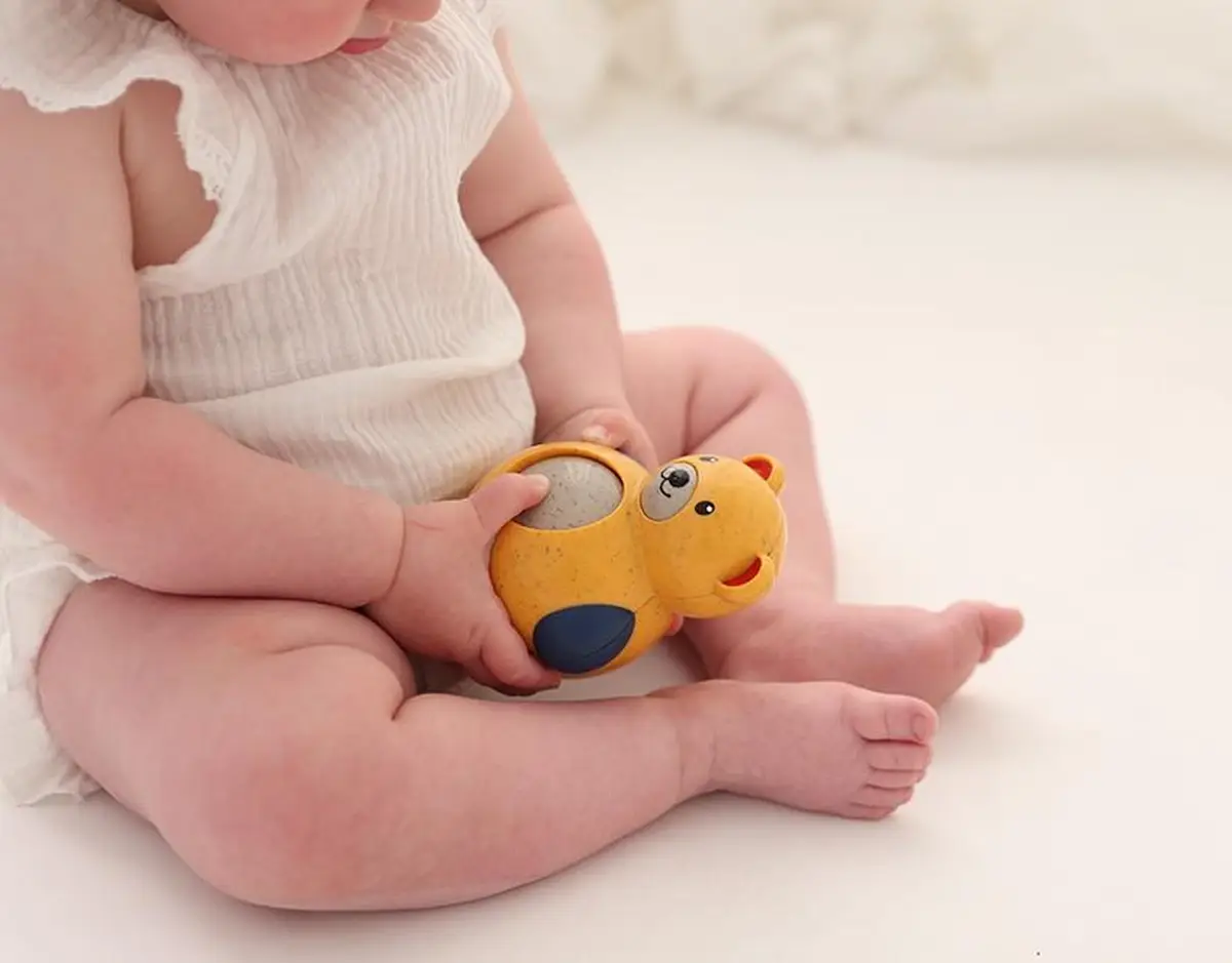 Niemowlę trzymające żółtego misia wańka wstańkę z niebieskimi łapkami dla dziecka powyżej 6 miesięcy. Tolo Bio Miś Roly Poly 6m+