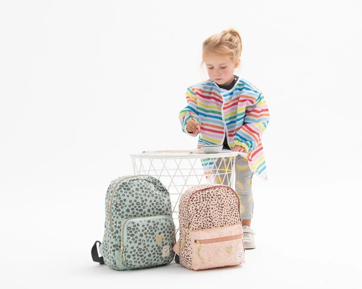 Dwa dziecięce plecaki w panterkę w kolorze miętowym i brzoskwiniowym obok małego dziecka malującego przy białym stoliku. Kidzroom Plecak dla dzieci Paris Growl peach