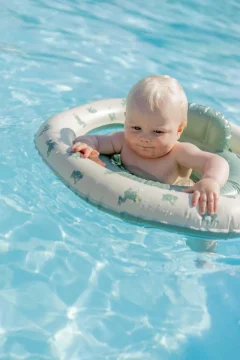 Niemowlę w jasnym kole do pływania z siedziskiem z motywem żabek na wodzie. Vanilla Copenhagen Koło do pływania Baby Fern Froggy z siedziskiem