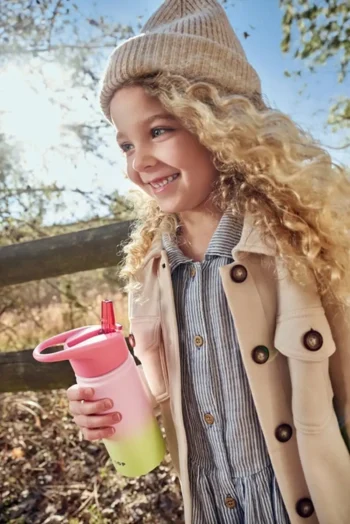 Dziecko trzyma termiczną butelkę z ustnikiem w kolorze ombre różowo-zielonym dla dziecka. Skip Hop Butelka Termiczna z Ustnikiem 450ml Ombre Pink Wander