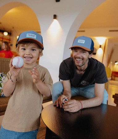 Dziecko i mężczyzna w niebieskich czapkach z daszkiem trzymający piłkę do baseballa i siedzący przy stole. Hello Hossy Mini Marine dad