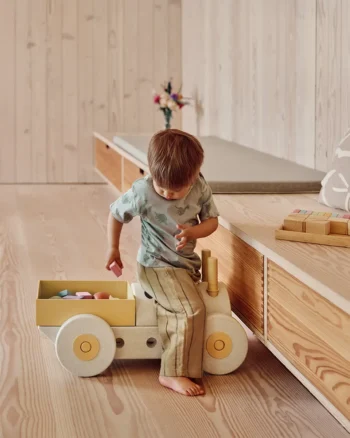 Dziecko siedzące na pchaczu 3w1 w kolorze szaro-żółtym z klockami piankowymi w skrzyni na zabawki. MODU Pchacz 3w1 Sand Grey / Honey Yellow