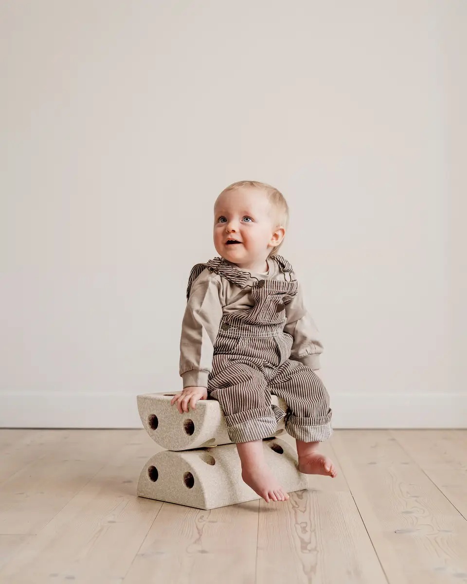Niemowlę siedzące na piankowym stołku w kolorze piaskowym na drewnianej podłodze dla dziecka. MODU Kids Stool Sand Grey / Honey Yellow