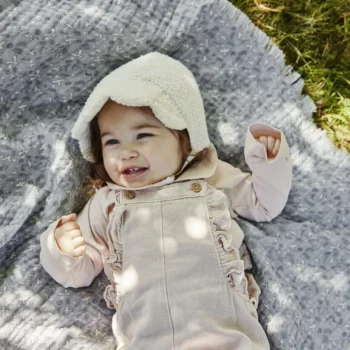 Niemowlę w białej czapce bouclé leżące na szarym kocyku z wzorem dla niemowlaka. Elodie Details Czapka Baby Bonnet White Bouclé 0-3 m-cy