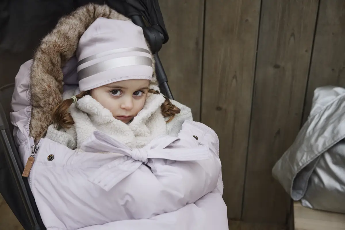 Dziecko w jasnofioletowej zimowej czapce z dwoma jasnoszarymi paskami dla dziecka 1-2 lata w wózku otulone jasnofioletowym śpiworem z futrzanym obszyciem. Elodie Details Czapka Lavender Love 1-2 lata