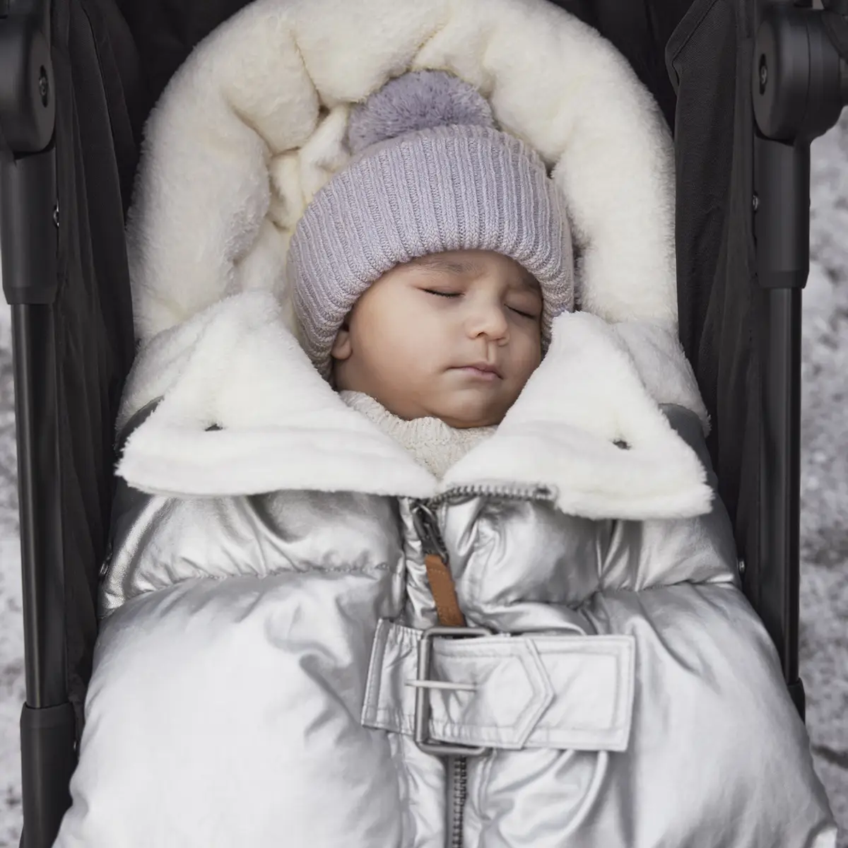 Niemowlę w jasnofioletowej wełnianej czapce z pomponem śpiące w srebrnym śpiworku w wózku zimowym. Elodie Details Czapka Wełniana Lavender Love 0-6 m-cy