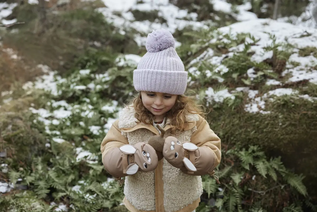 Dziewczynka w jasnofioletowej wełnianej czapce zimowej z pomponem w lesie zimą dla dziecka. Elodie Details Czapka Wełniana Lavender Love 3-100 lat