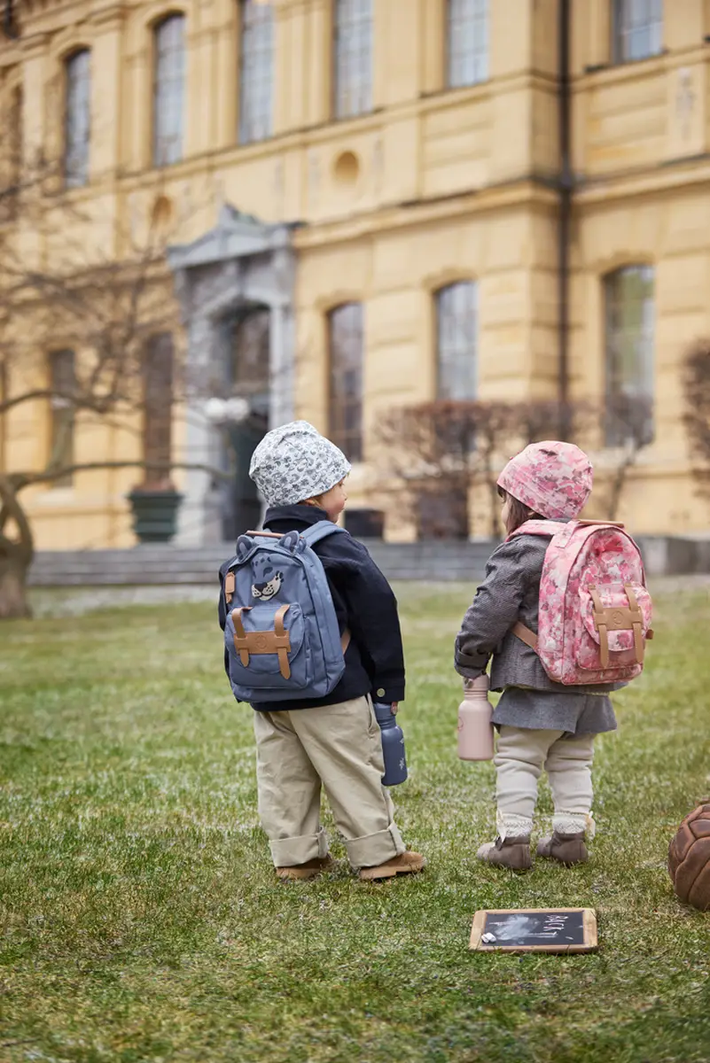 Dziecko trzymające różową butelkę na wodę w kwiatowy wzór dla dziecka na tle budynku. Elodie Details Butelka na wodę Garden Leo