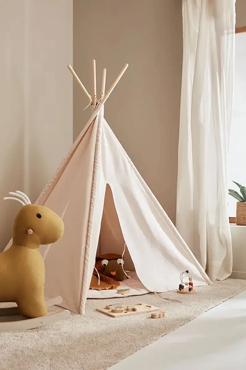 Biały namiot tipi z drewnianymi kijami dla dziecka w pokoju zabaw z pluszową zabawką i drewnianymi układankami na dywanie. Kid’s Concept Namiot Tipi off white