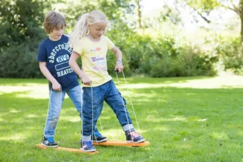 Dzieci bawiące się na zewnątrz na pomarańczowej równoważni narty do zabawy na trawie. BS Toys Gra Narty równoważnia