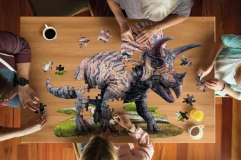 Układanie puzzli z obrazem triceratopsa na drewnianym stole z udziałem kilku osób. Madd Capp Puzzle Konturowe Triceratops 100 Elementów