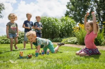 Dzieci bawiące się na trawie drewnianą grą zręcznościową z króliczkami na zewnątrz. BS Toys Drewniana gra zręcznościowa Króliczki