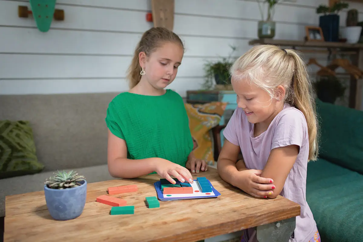 Dwie dziewczynki grające w drewnianą łamigłówkę zakryj kropki na stole w pokoju dziecięcym. BS Toys drewniana gra logiczna Łamigłówka zakryj kropki