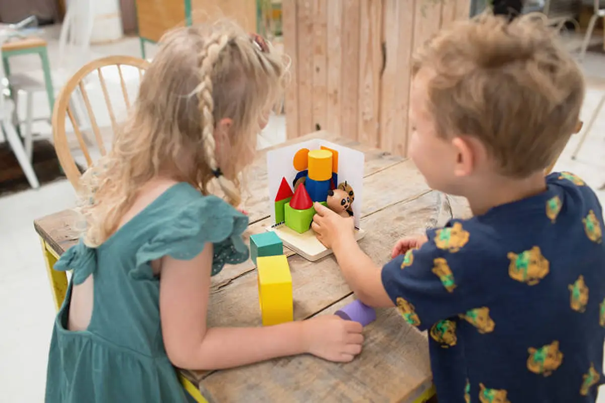 Dzieci bawiące się drewnianą łamigłówką 3D panda z kolorowymi klockami na drewnianym stole. BS Toys drewniana gra logiczna Łamigłówka puzzle 3D Panda