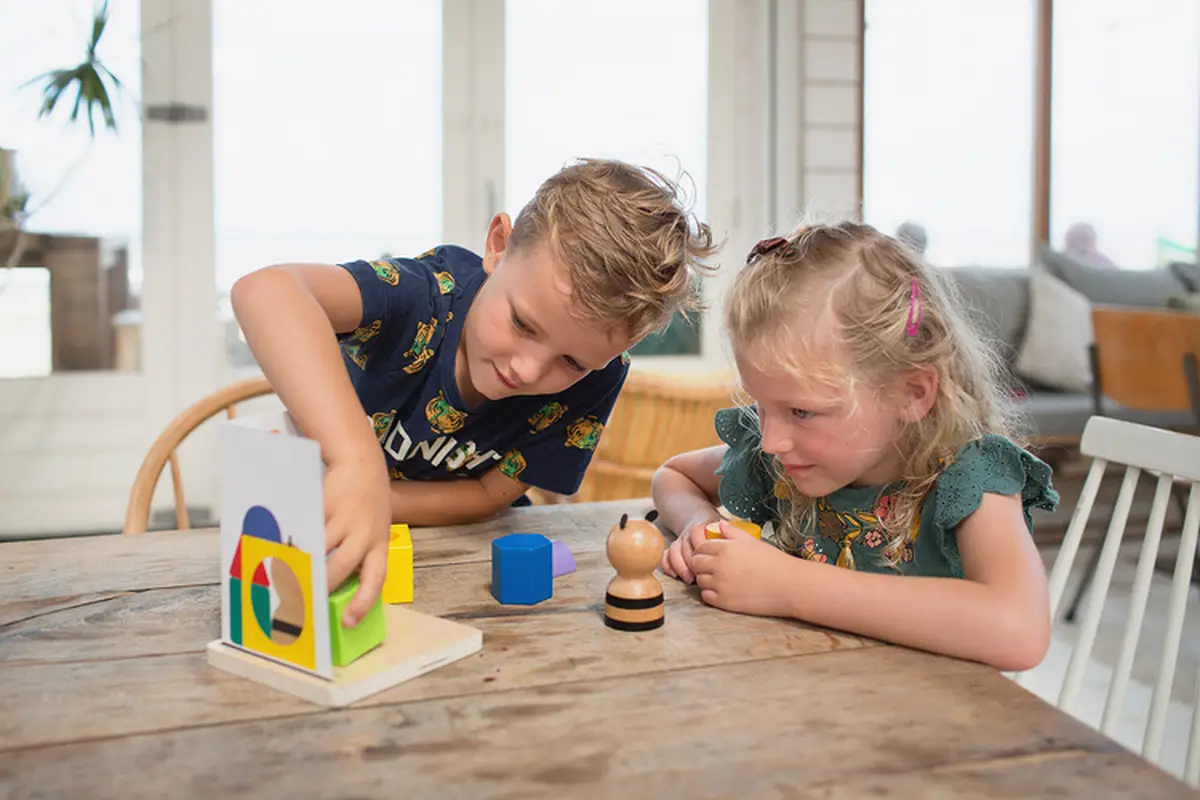 Dwoje dzieci bawiących się drewnianymi zabawkami edukacyjnymi na stole w jasnym pomieszczeniu. BS Toys drewniana gra logiczna Łamigłówka puzzle 3D Panda